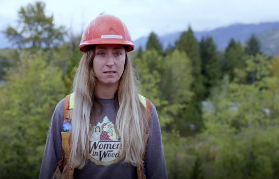 Woman wearing safety gear looking at the camera with forest in the background.