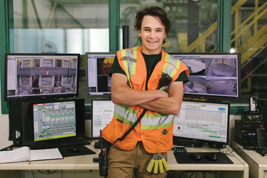 Person in safety gear in front of computer screens in a pellet mill.